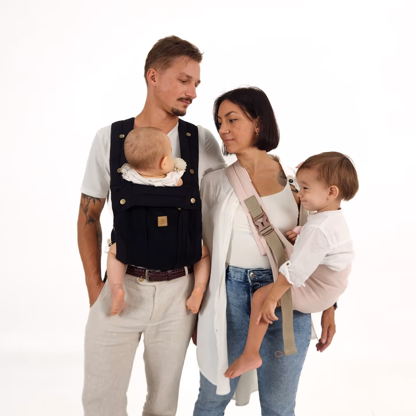 A family using a black baby carrier, with the baby securely positioned in the carrier, shown in a home setting.