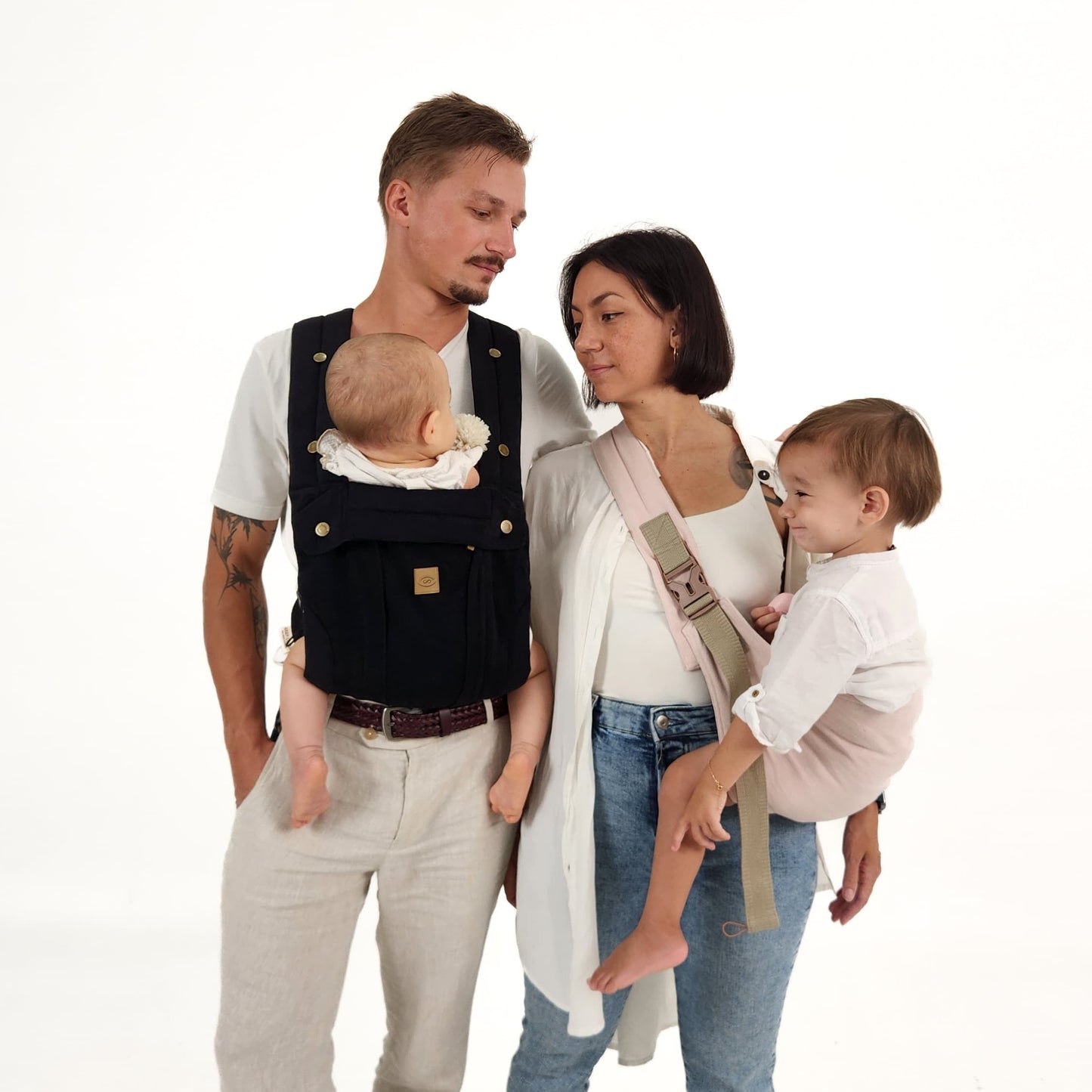 A family using a black baby carrier, with the baby securely positioned in the carrier, shown in a home setting.