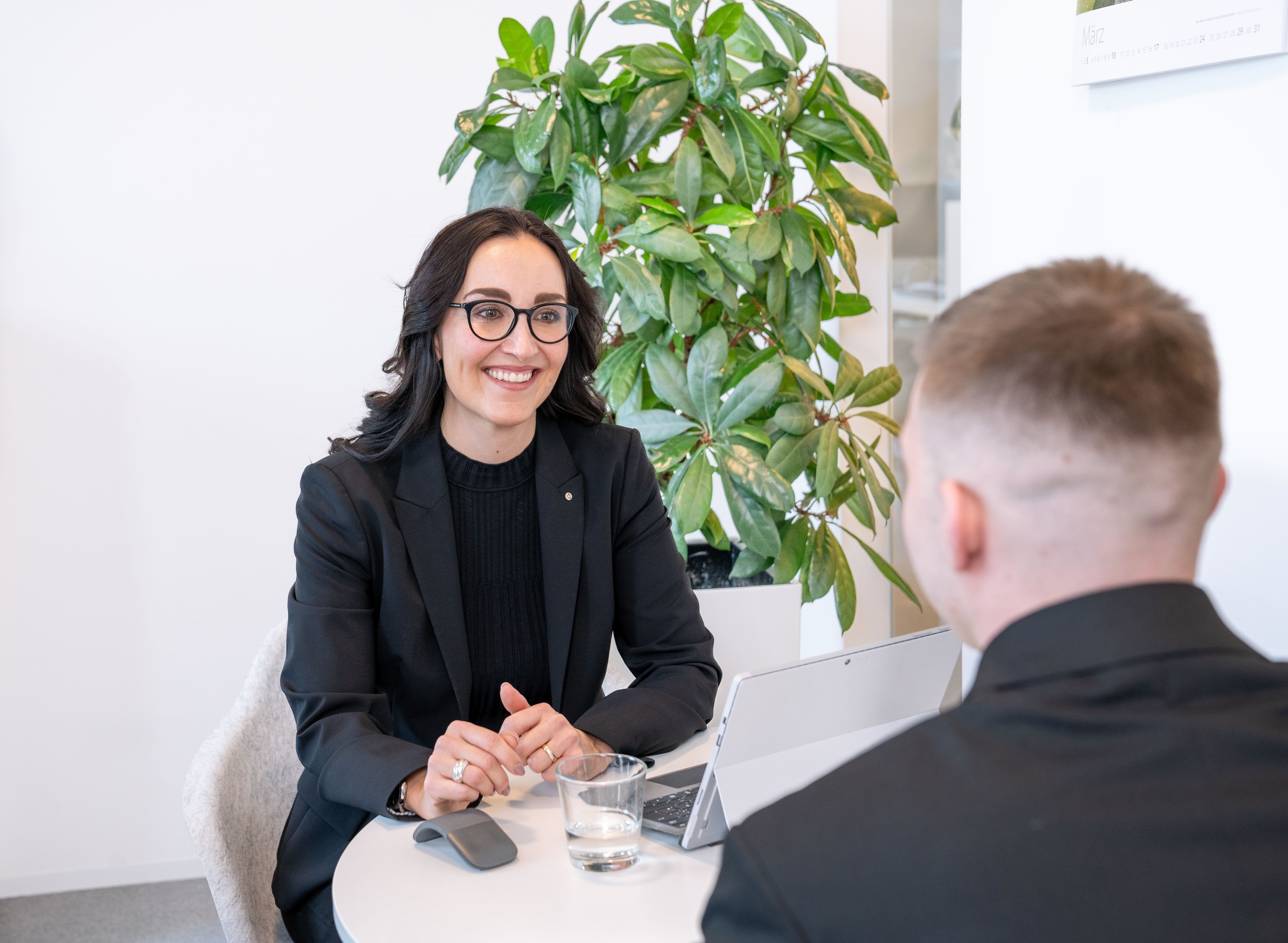 Frau im schwarzen Outfit sitzt im Gespräch mit zwei Personen im Büro.