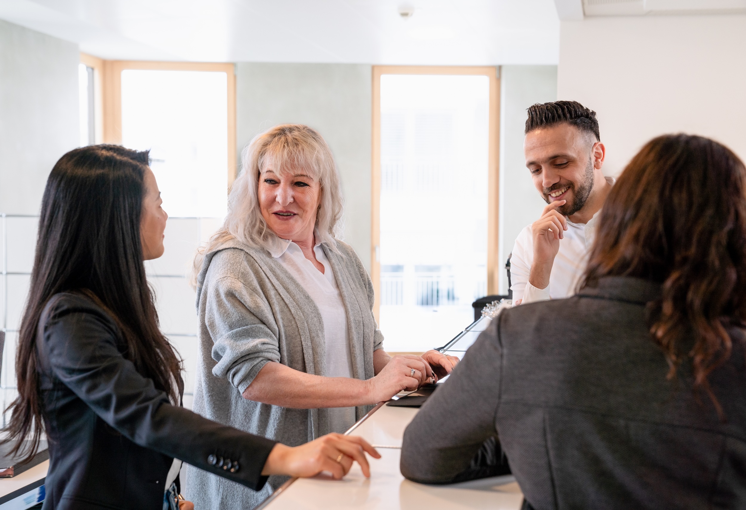 Meeting-Situation im Büro, mehrere Personen sitzen am Tisch und sprechen.