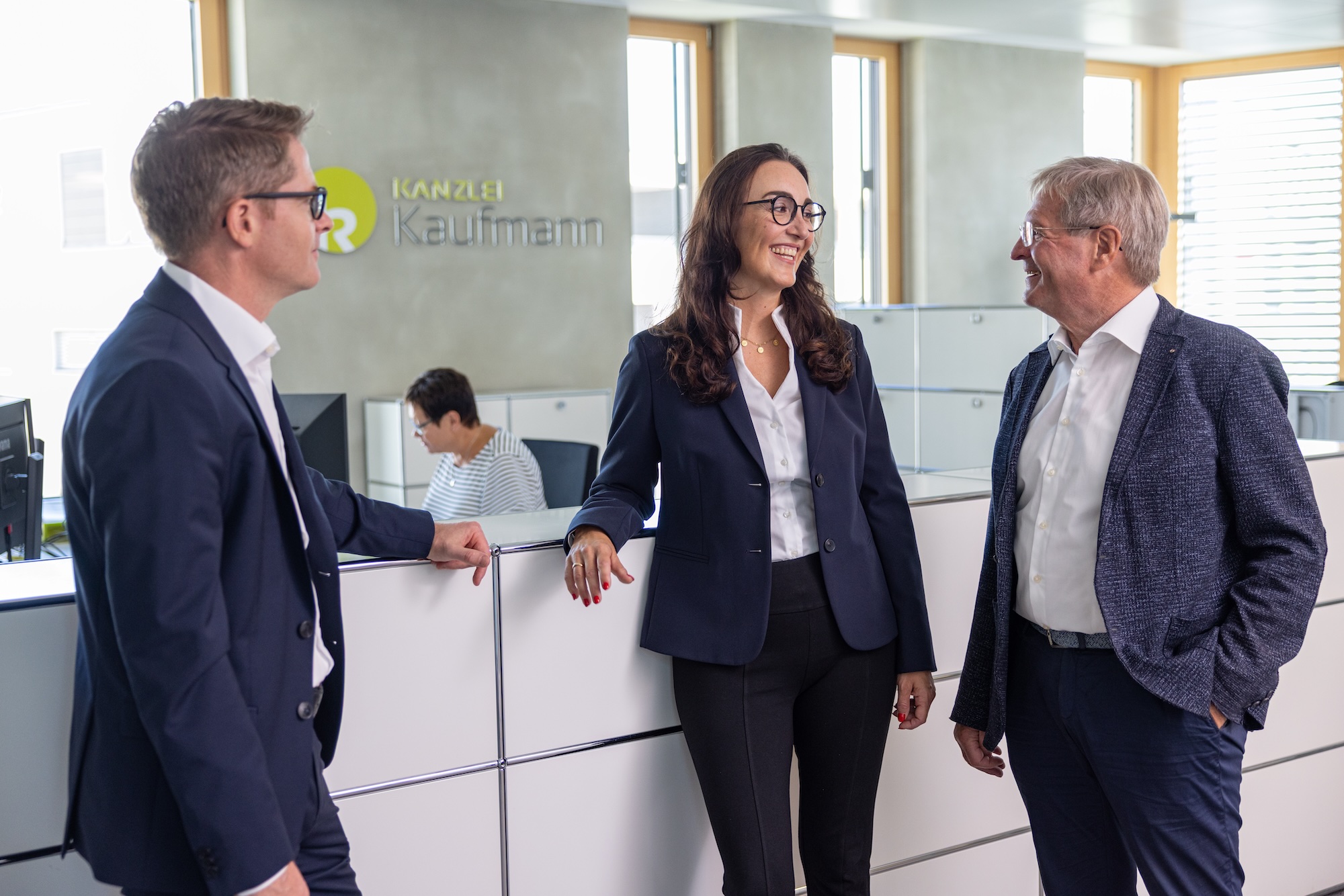 Drei Personen im Büro im Gespräch, eine Person hält Unterlagen.
