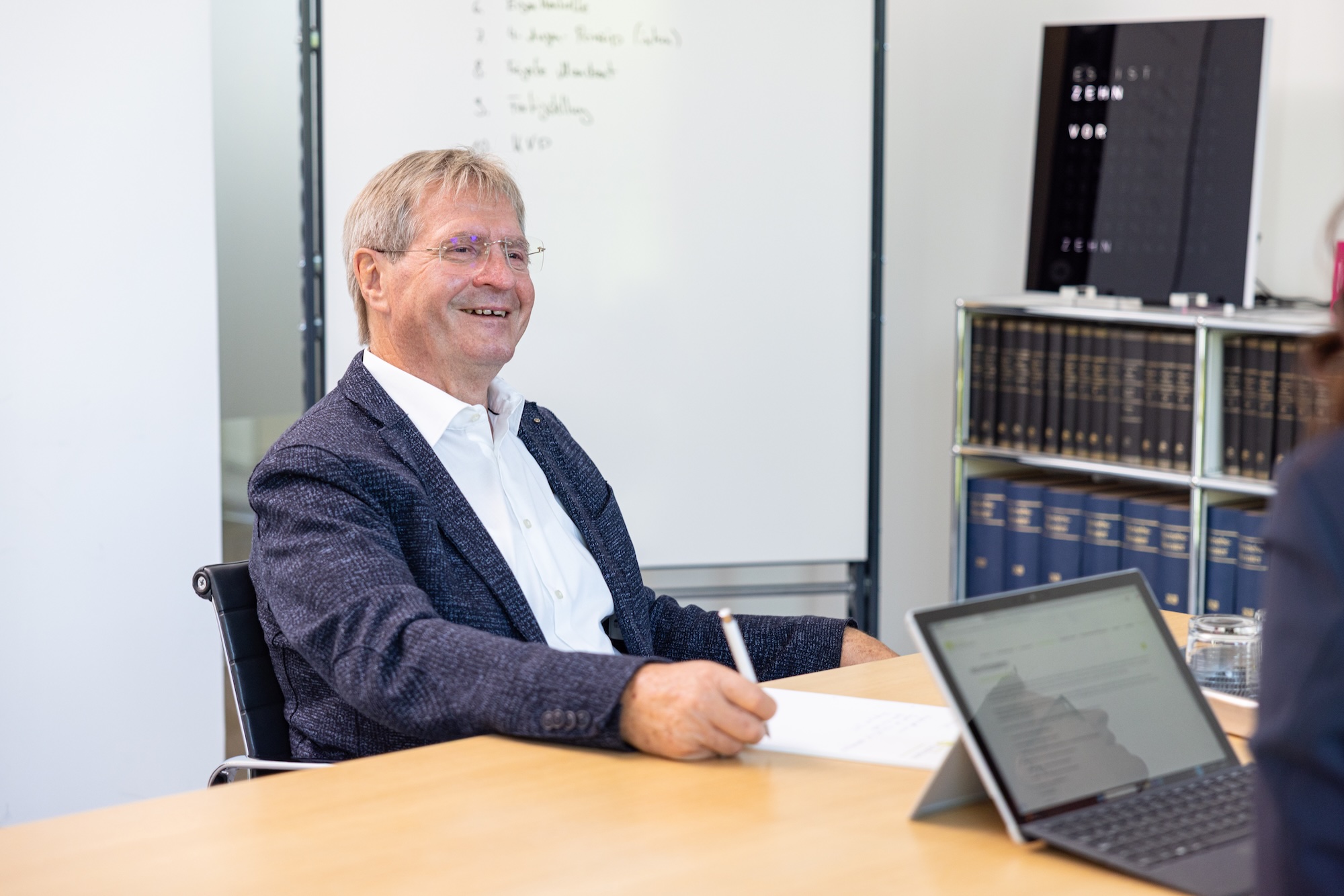 Mann im Anzug sitzt am Tisch im Büro und lächelt.