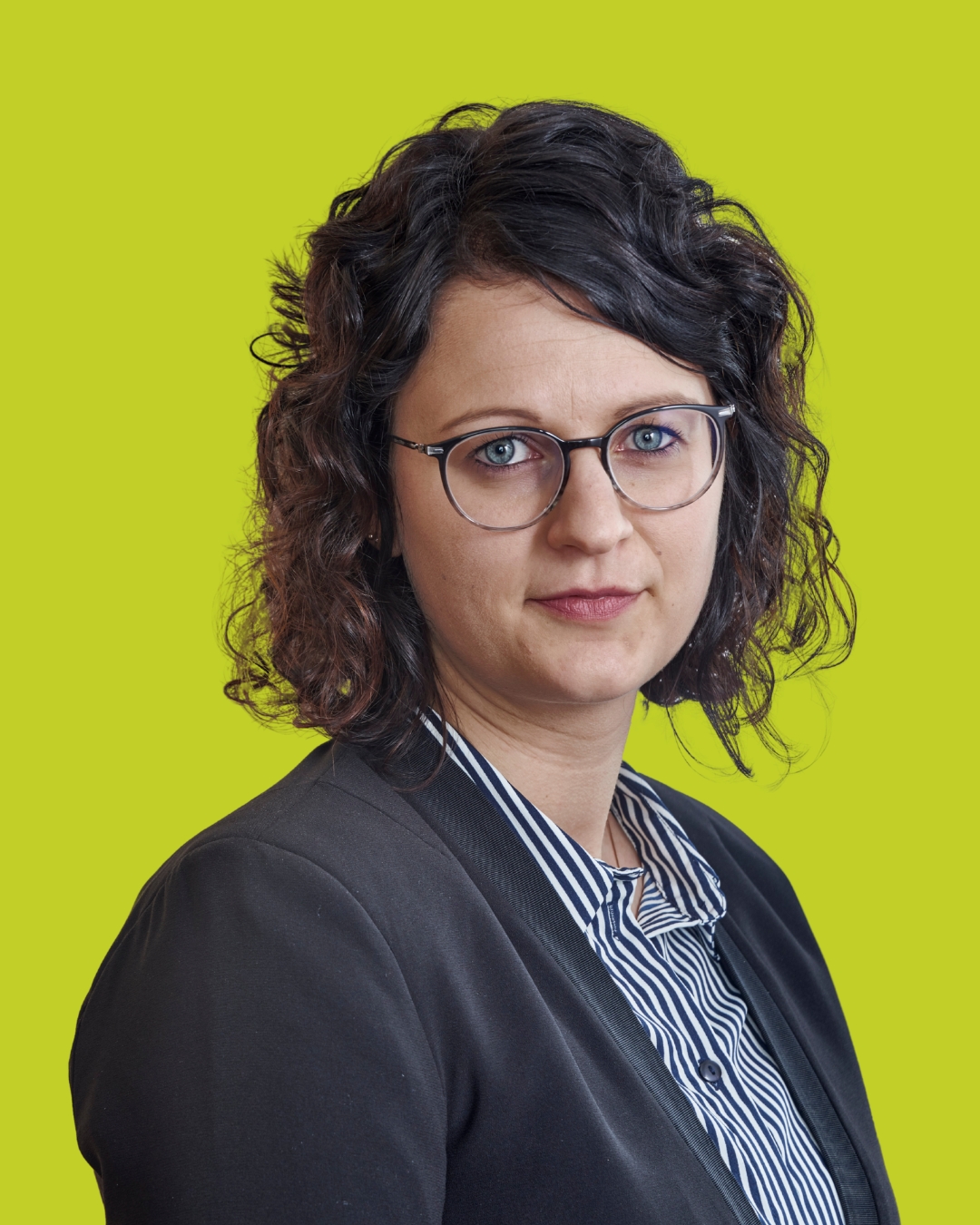 Porträt einer Frau mit Brille im Blazer vor grünem Hintergrund.