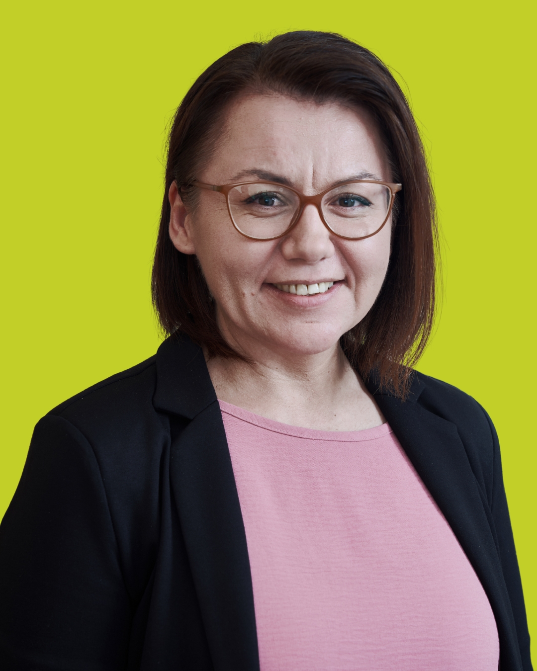 Porträt einer Frau mit Brille im Blazer vor grünem Hintergrund.