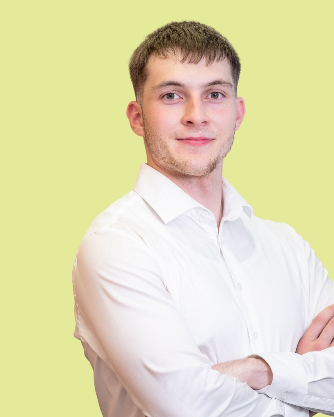 Porträt eines jungen Mannes im weißen Hemd mit verschränkten Armen vor grünem Hintergrund.