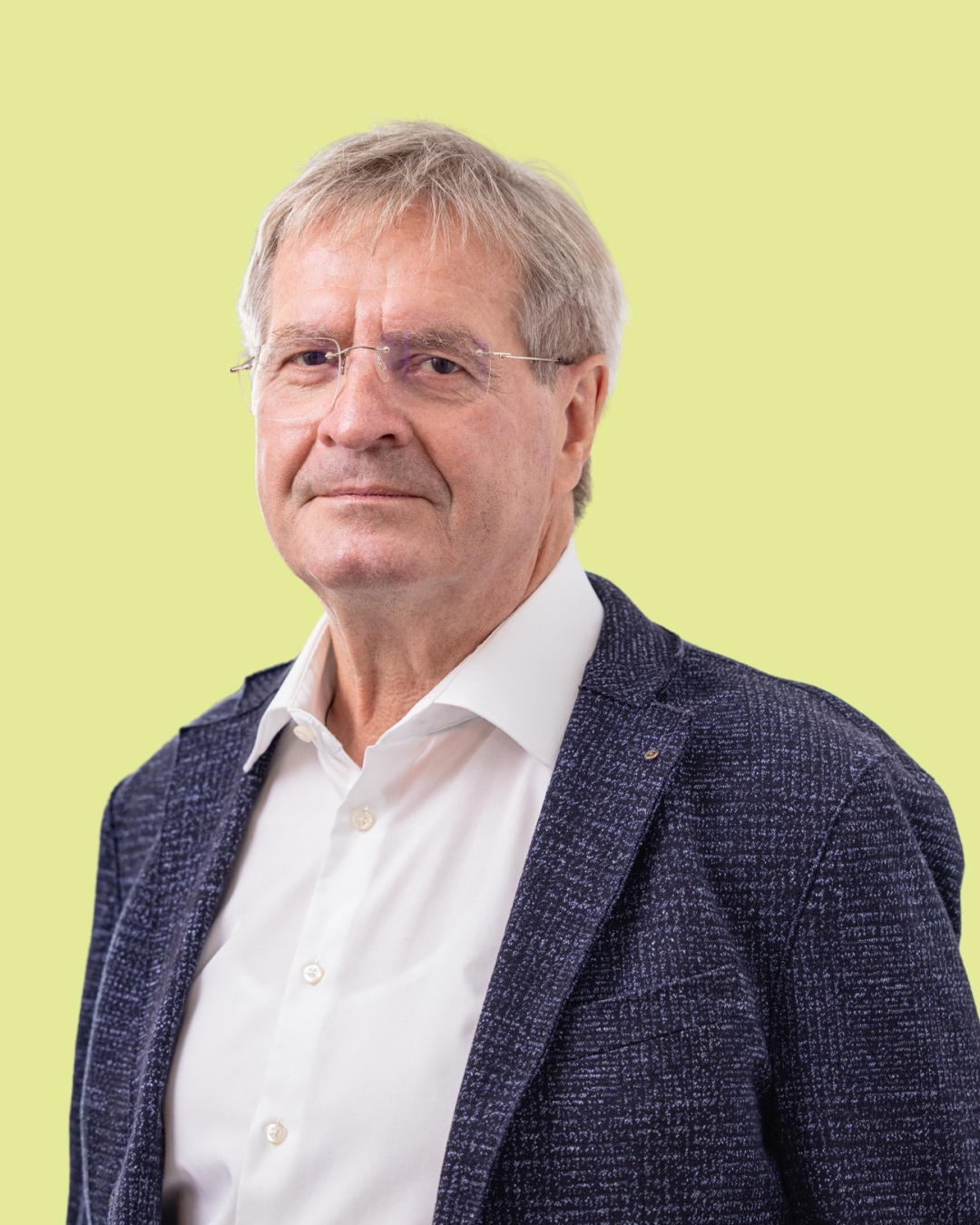 Porträt eines älteren Mannes im Sakko vor grünem Hintergrund.