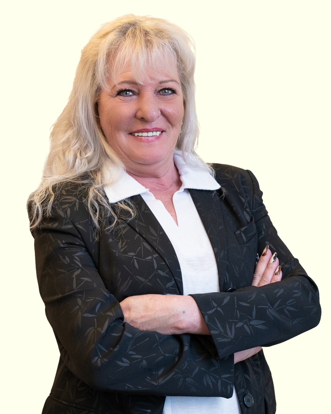 Porträt einer Frau im Business-Outfit mit verschränkten Armen vor hellem Hintergrund.