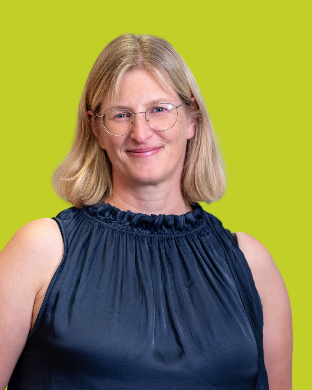 Porträt einer Frau im ärmellosen dunklen Oberteil vor grünem Hintergrund.