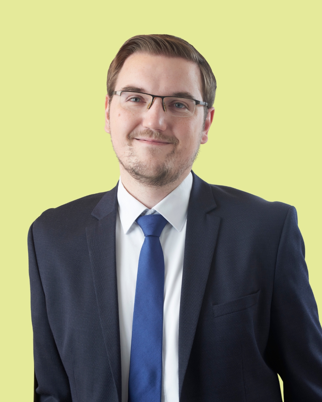 Porträt eines Mannes mit Brille im Anzug vor grünem Hintergrund.