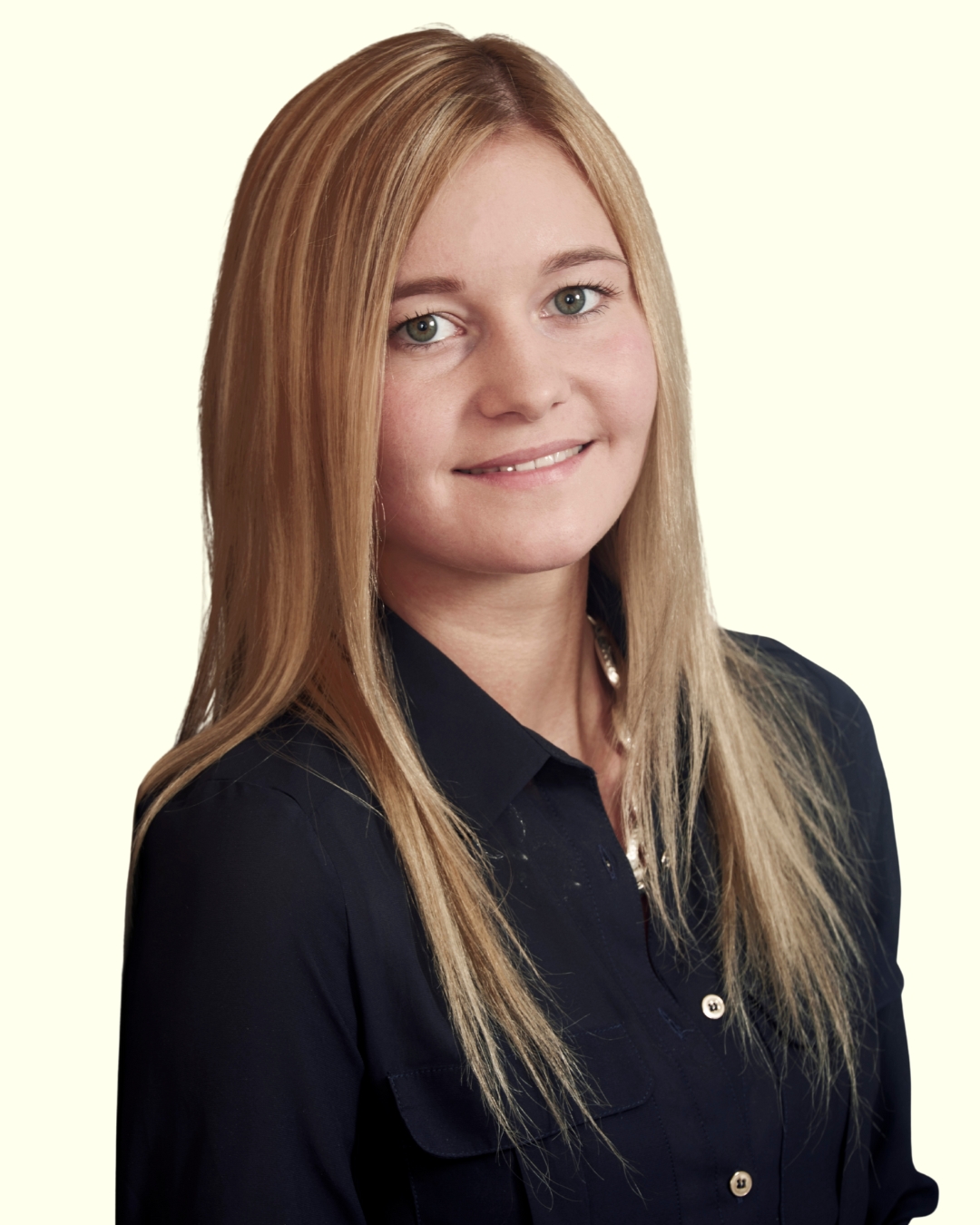 Porträt einer jungen Frau mit langen blonden Haaren vor hellem Hintergrund.