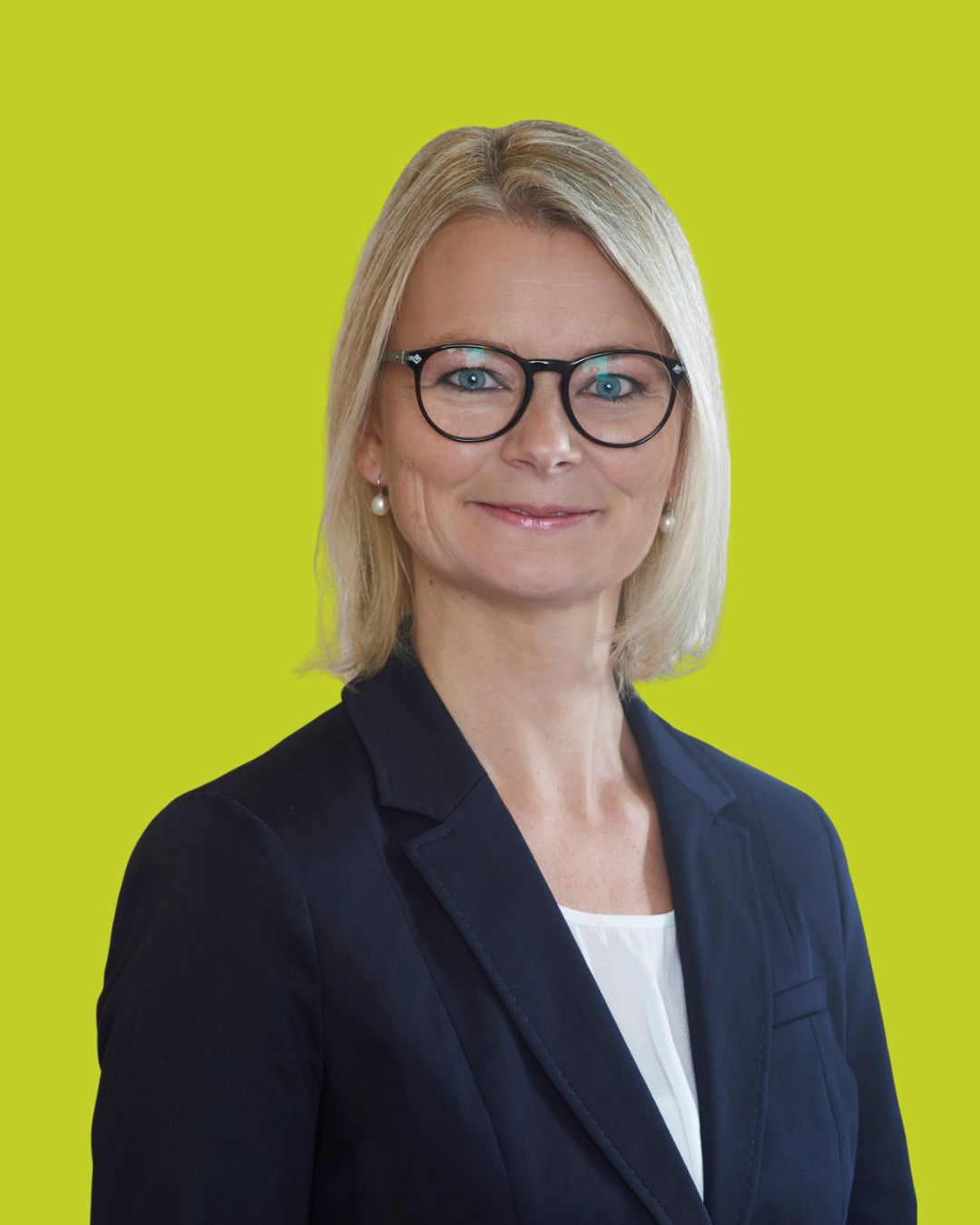 Porträt einer Frau mit Brille im Blazer vor grünem Hintergrund.