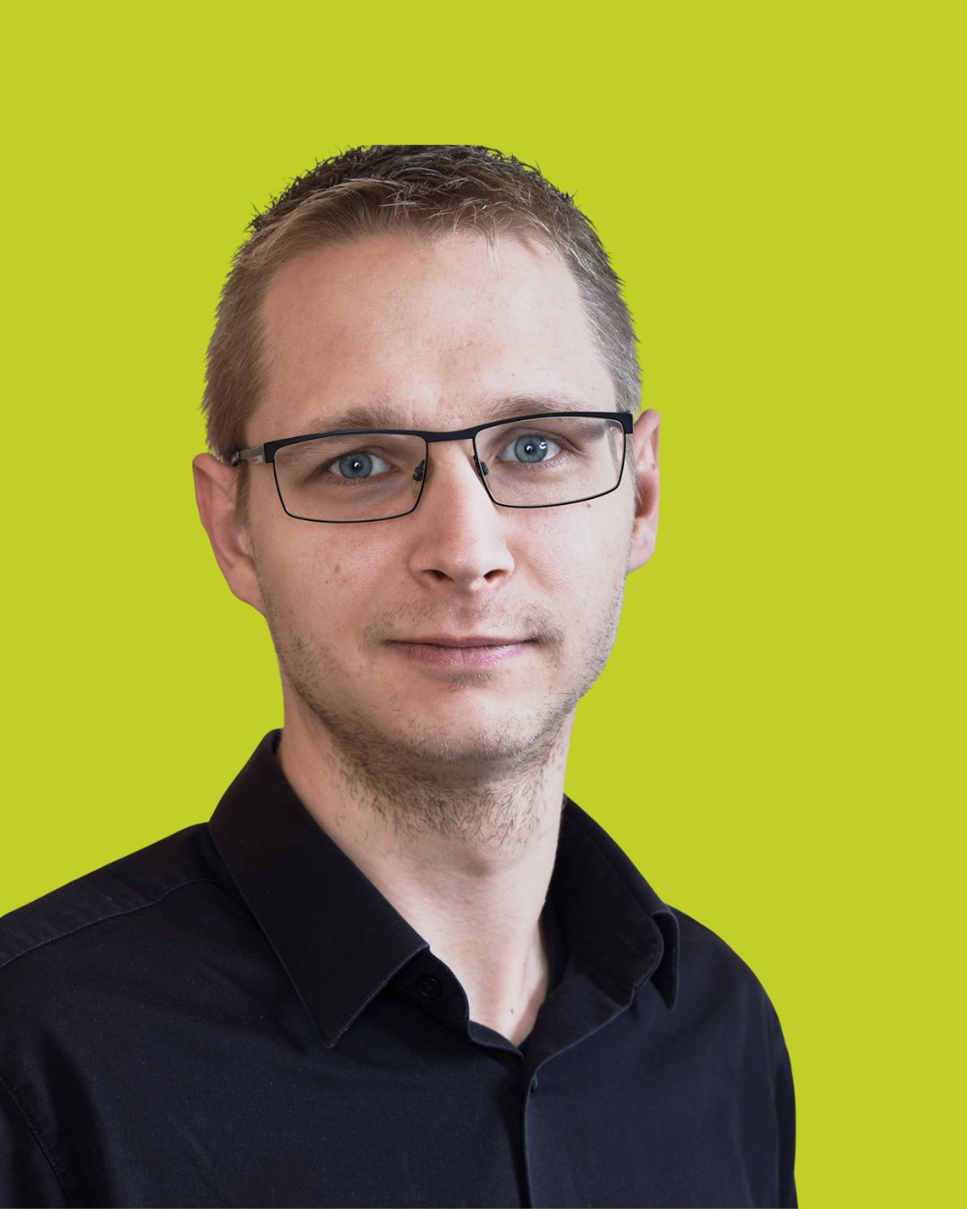 Porträt eines Mannes mit Brille im dunklen Hemd vor grünem Hintergrund.