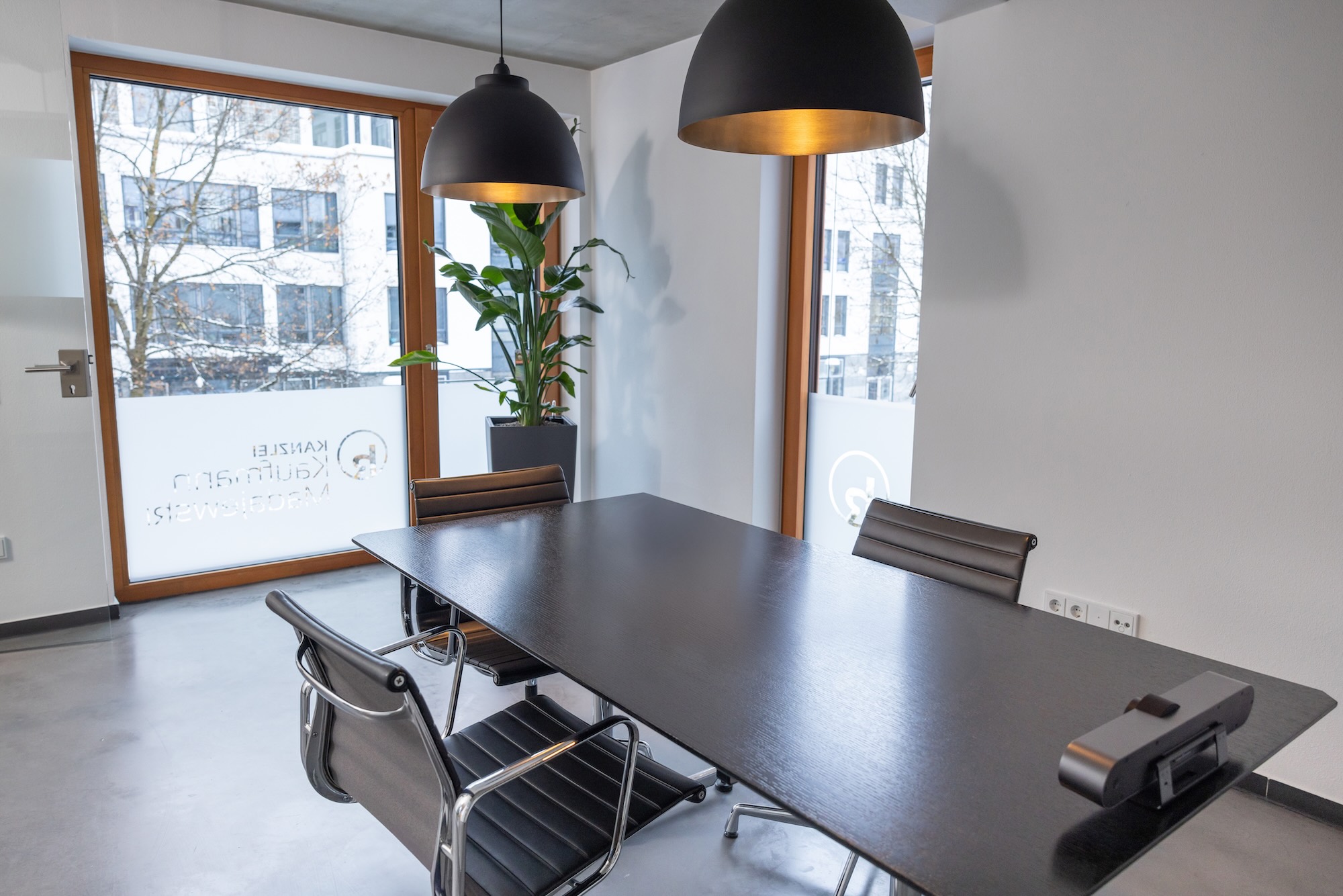 Besprechungsraum mit großem Tisch, Pflanzen und Lampen.