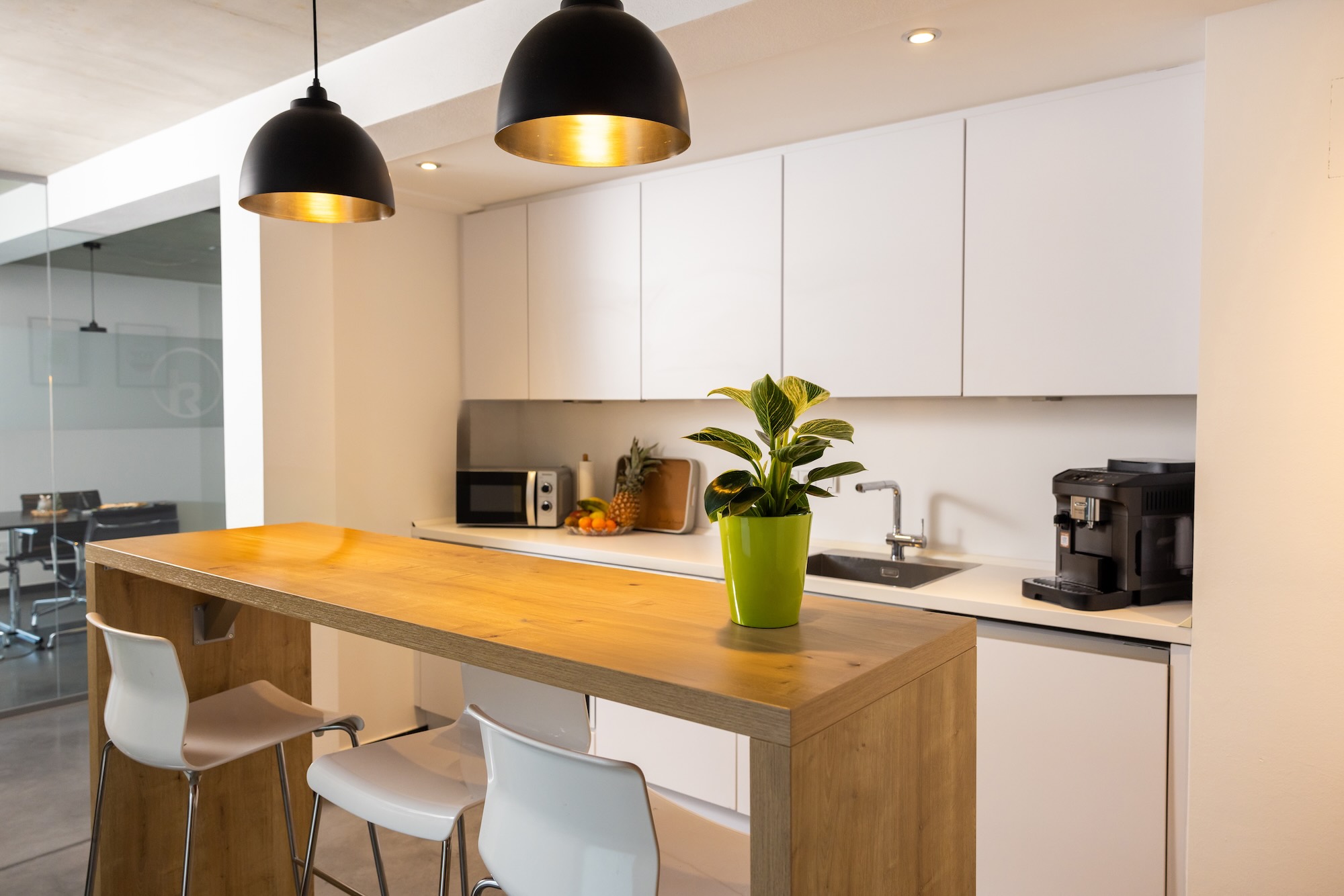 Moderne Büroküche mit Kochinsel, Barhockern und Pflanzen.