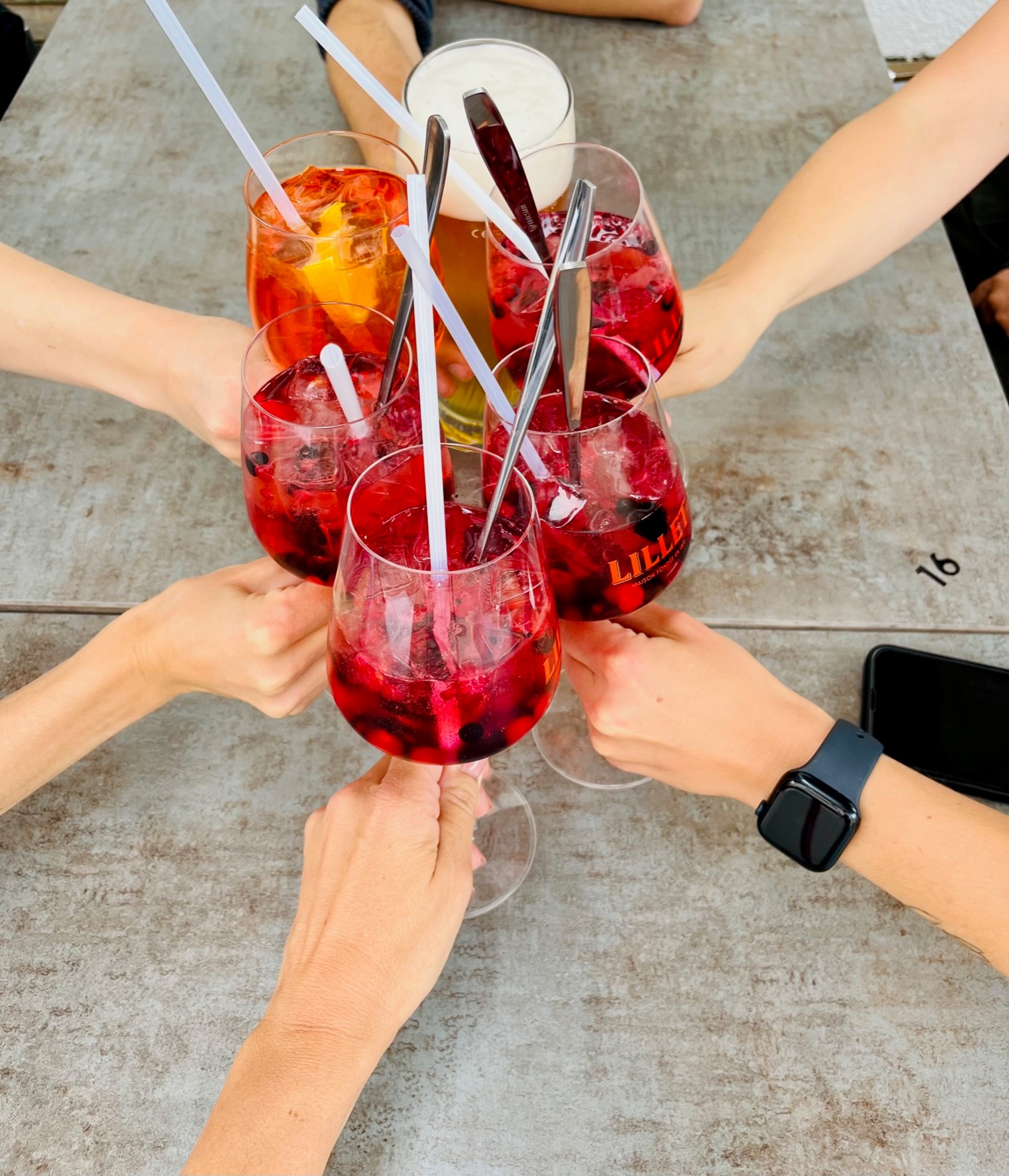 Mehrere Hände stoßen mit Gläsern mit rotem Getränk an (After-Work).