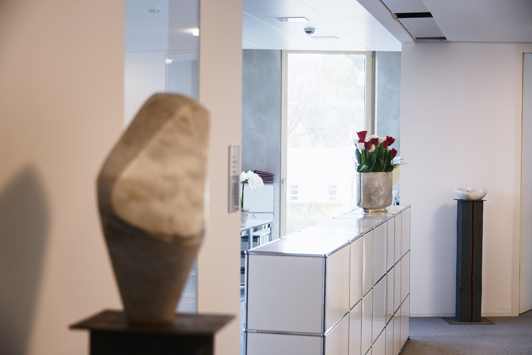Büro-Interior mit Skulptur auf Podest und Empfangsbereich im Hintergrund.