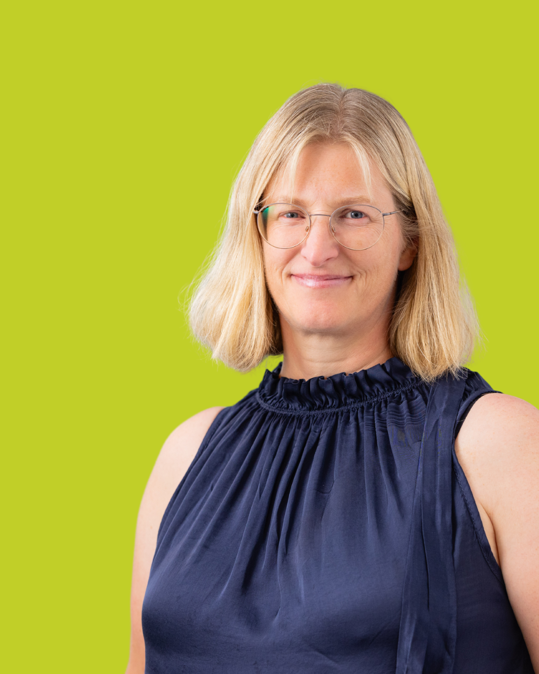 Porträt einer Frau im ärmellosen dunklen Oberteil vor grünem Hintergrund.