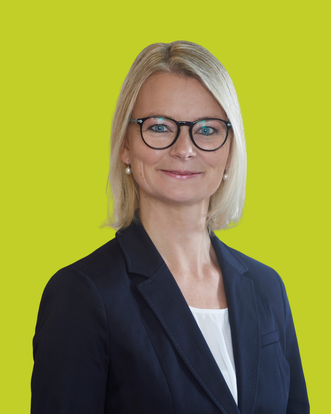 Porträt einer Frau mit Brille im Blazer vor grünem Hintergrund.