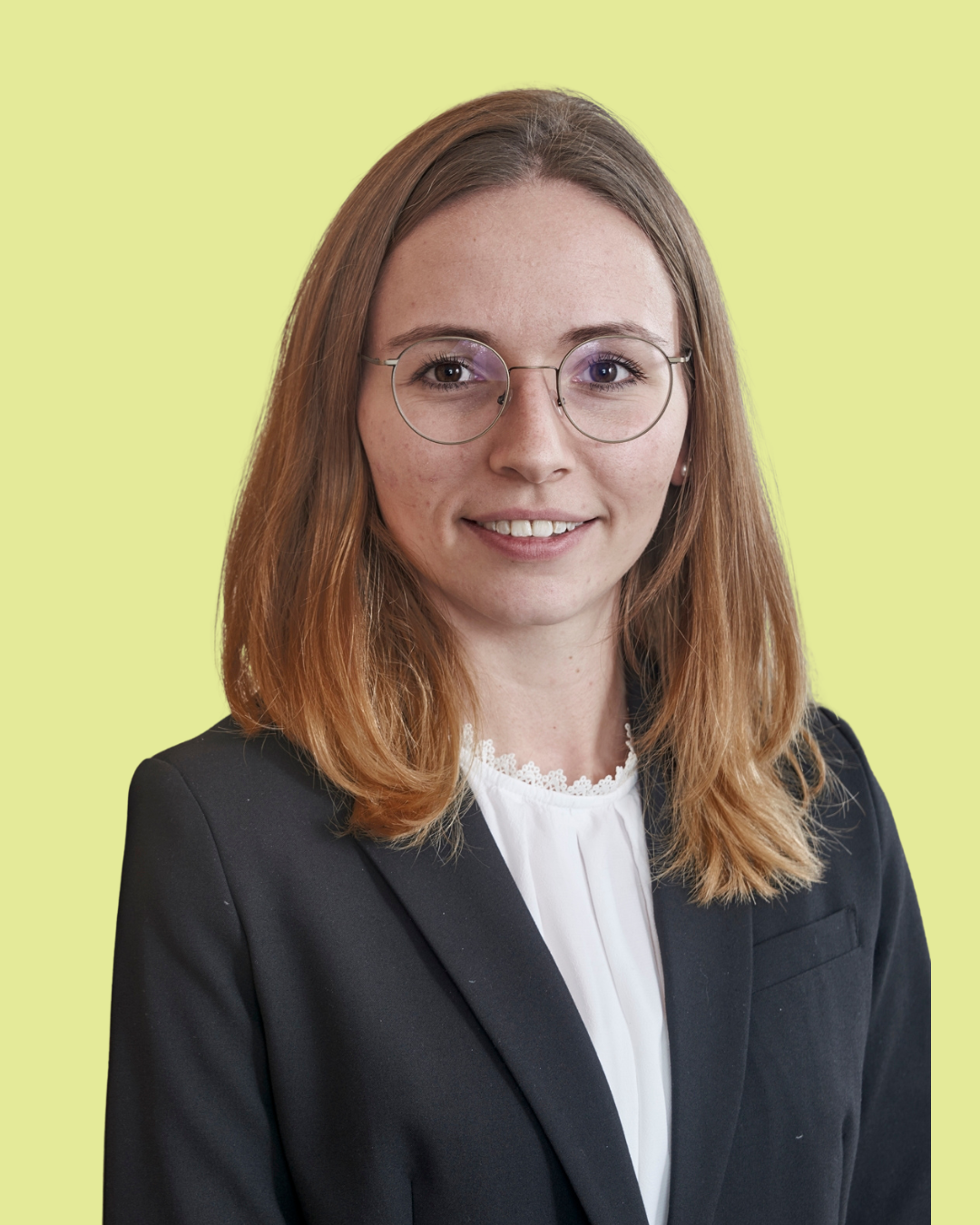 Porträt einer jungen Frau mit Brille im Business-Outfit vor grünem Hintergrund.