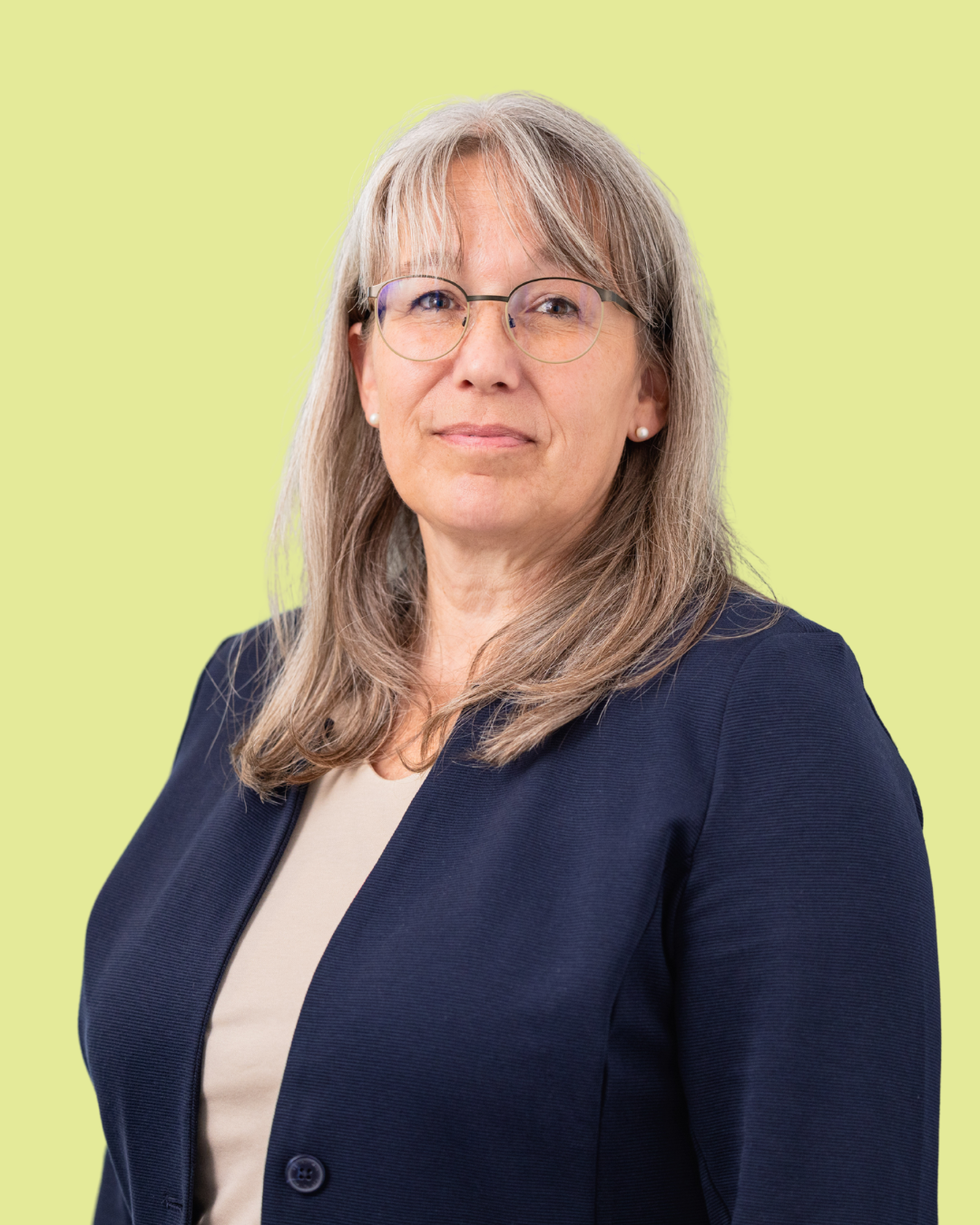 Porträt einer Frau mit langen grauen Haaren im Business-Outfit vor grünem Hintergrund.