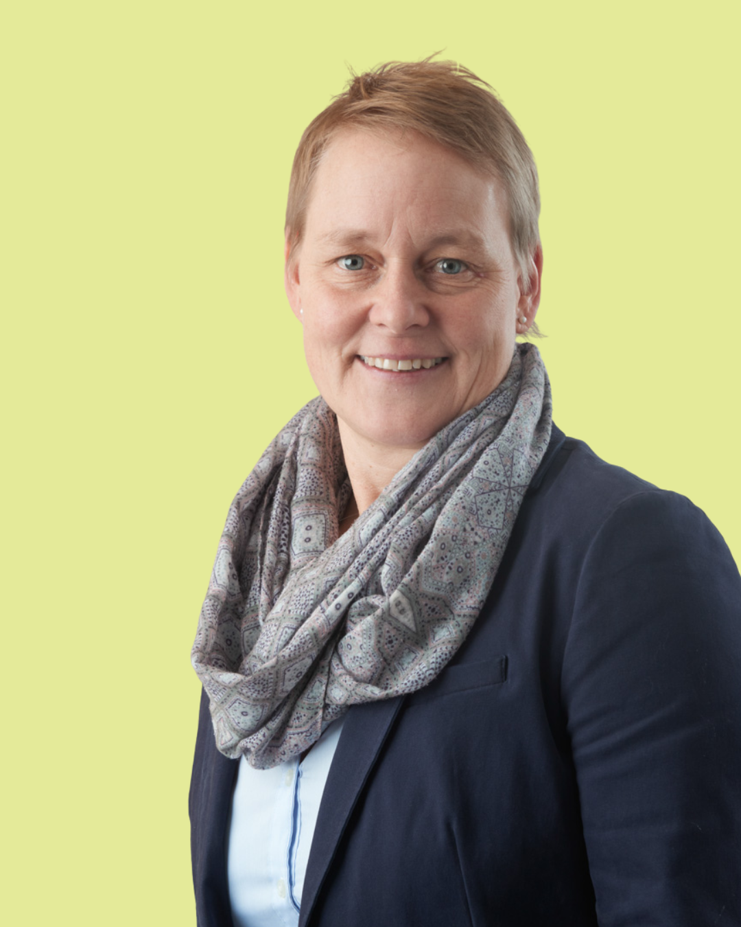 Porträt einer Frau im Blazer mit Schal vor grünem Hintergrund.