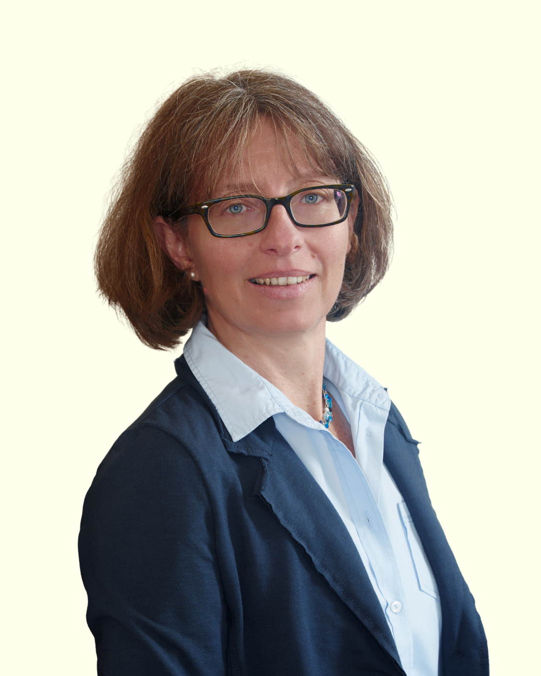 Porträt einer Frau mit Brille im Business-Outfit vor hellem Hintergrund.