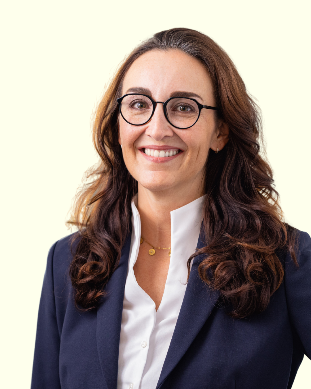 Porträt einer Frau mit Brille im Blazer vor hellem Hintergrund.