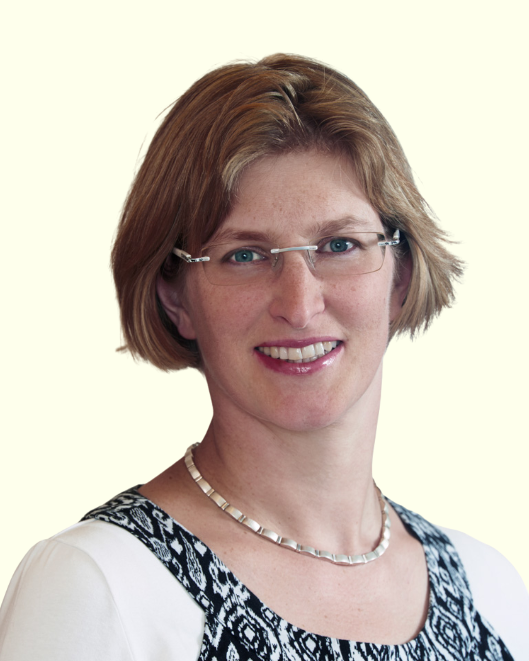 Porträt einer Frau mit Brille und Halskette vor hellem Hintergrund.