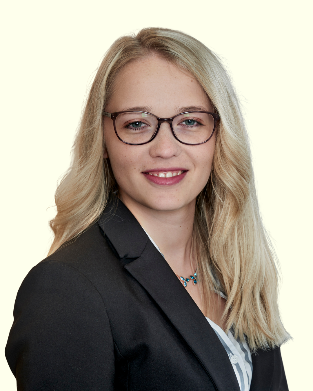 Porträt einer Frau mit Brille im Business-Outfit vor hellem Hintergrund.