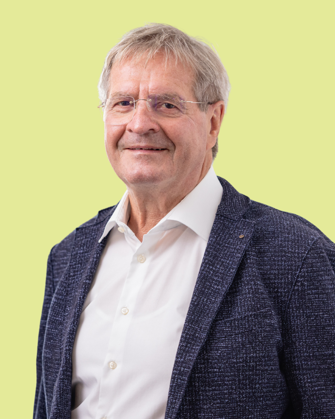 Porträt eines älteren Mannes im Sakko vor grünem Hintergrund.