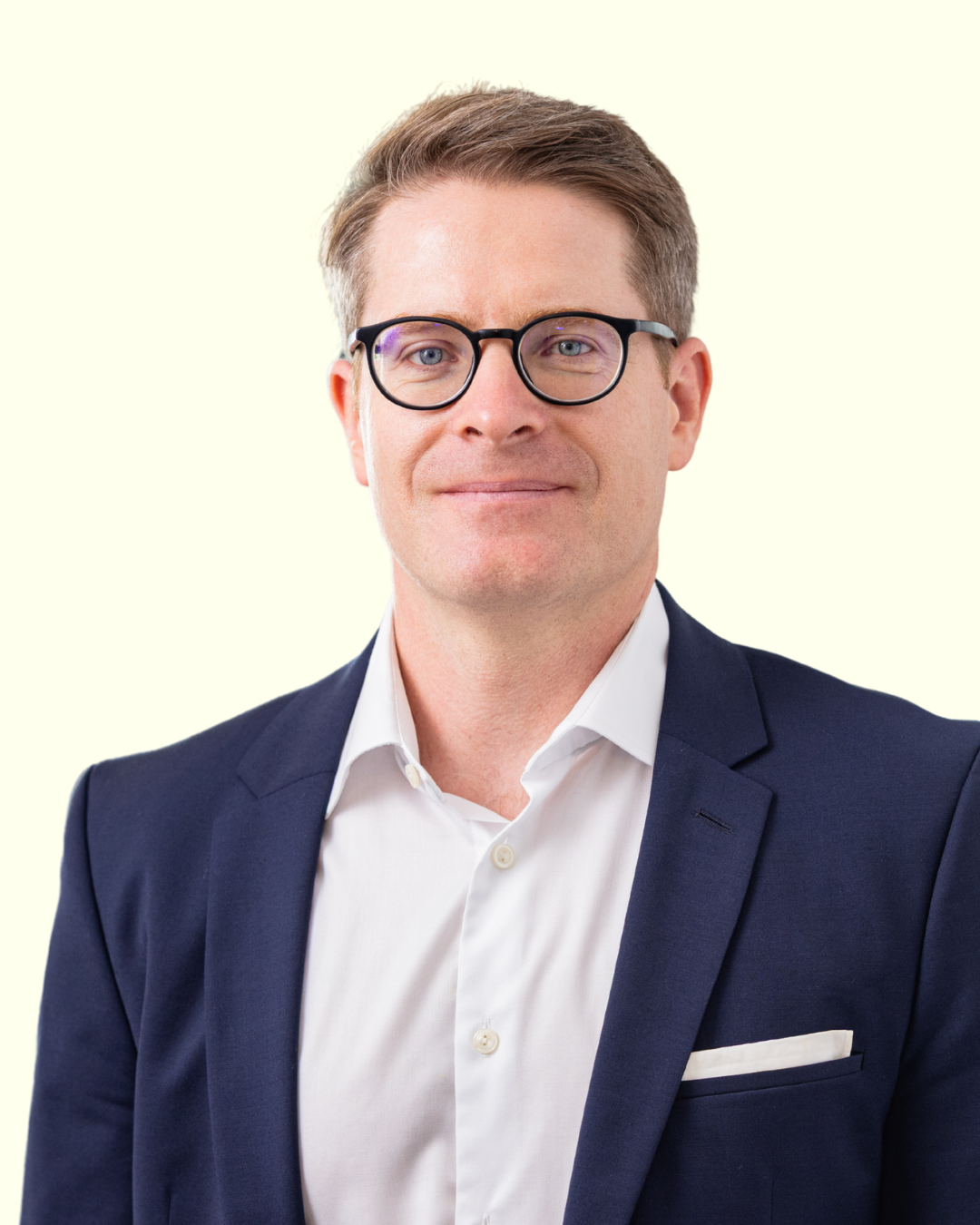 Porträt eines Mannes mit Brille im Anzug vor hellem Hintergrund.