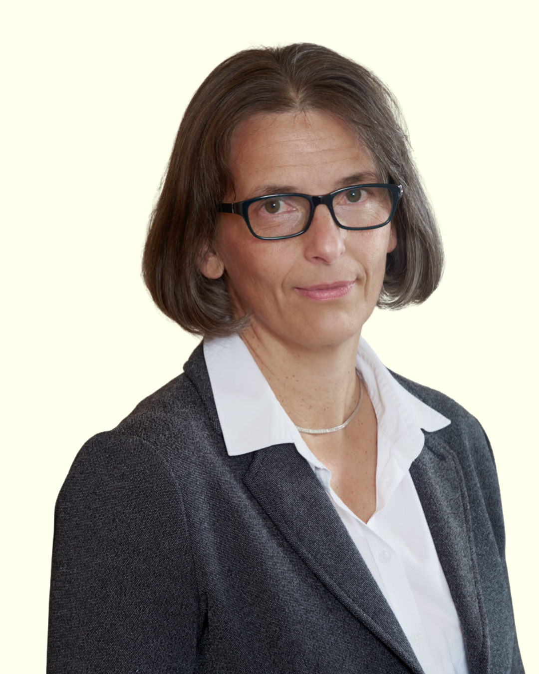 Porträt einer Frau mit Brille im Business-Outfit vor hellem Hintergrund.