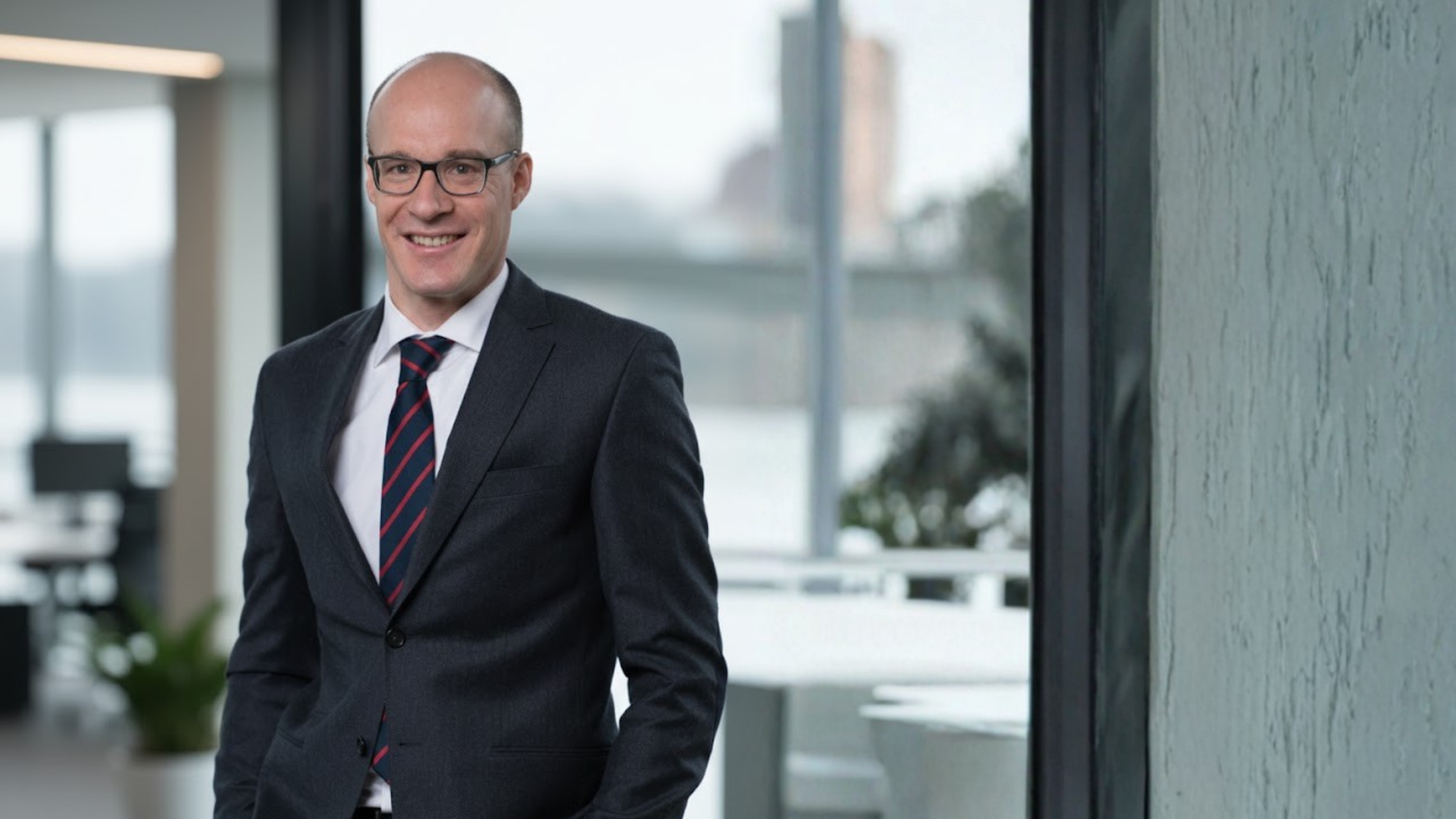 Porträt eines Mannes im Anzug vor modernem Büro-Hintergrund.