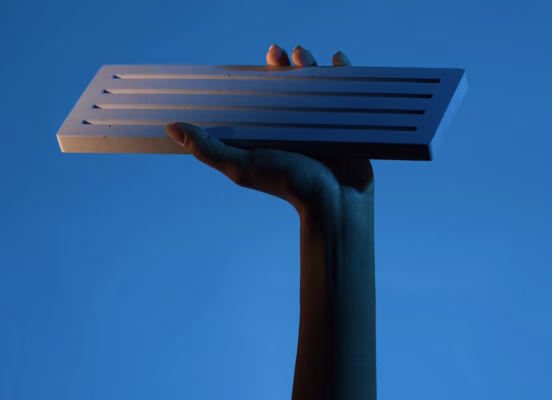 Hand holding a rectangular white object with multiple horizontal black slits against a blue background.