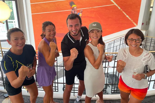 Group of five people posing with fists raised in front of a tennis poster.
