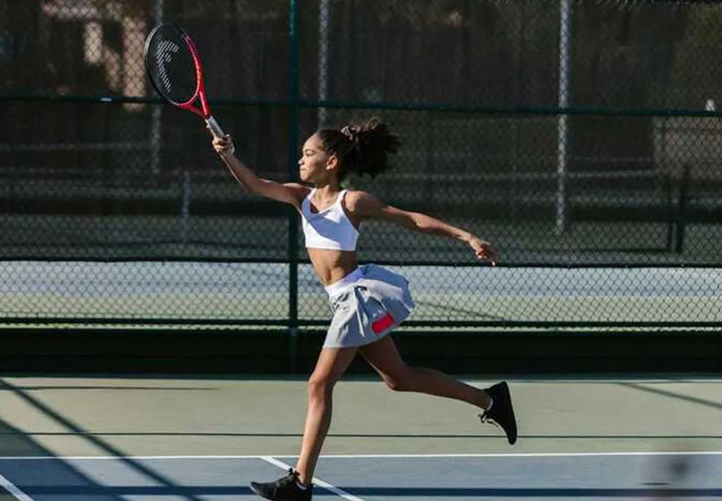 A young girl running on a tennis court with her racket raised.