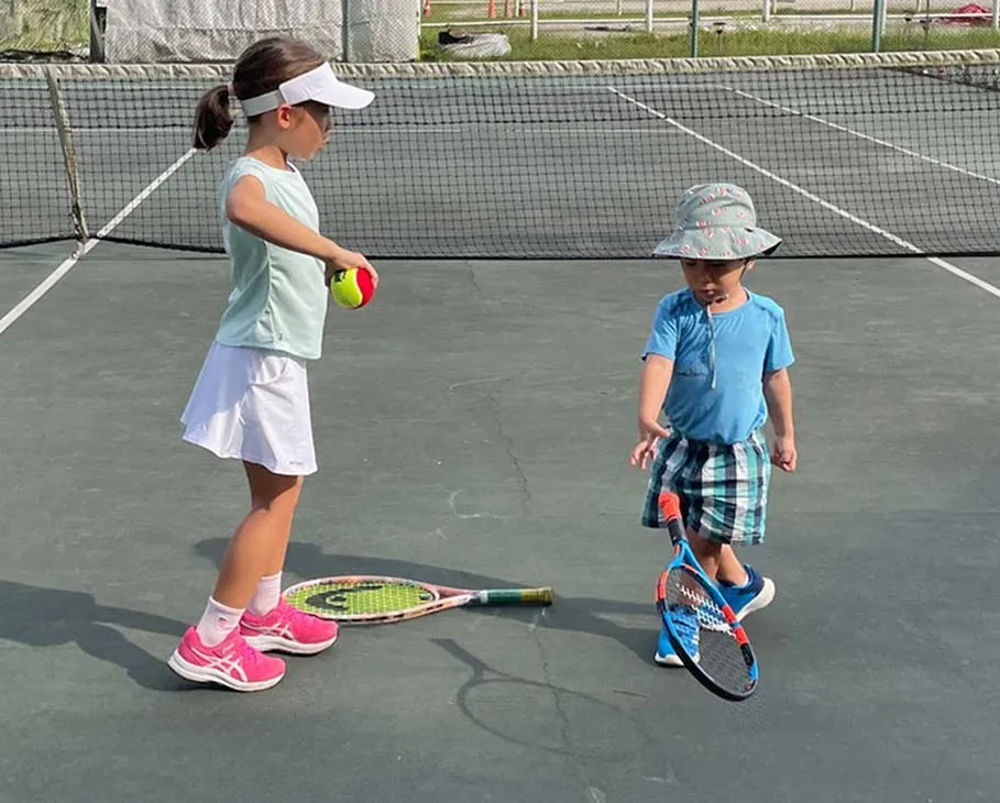 Two children with tennis rackets on the tennis court.