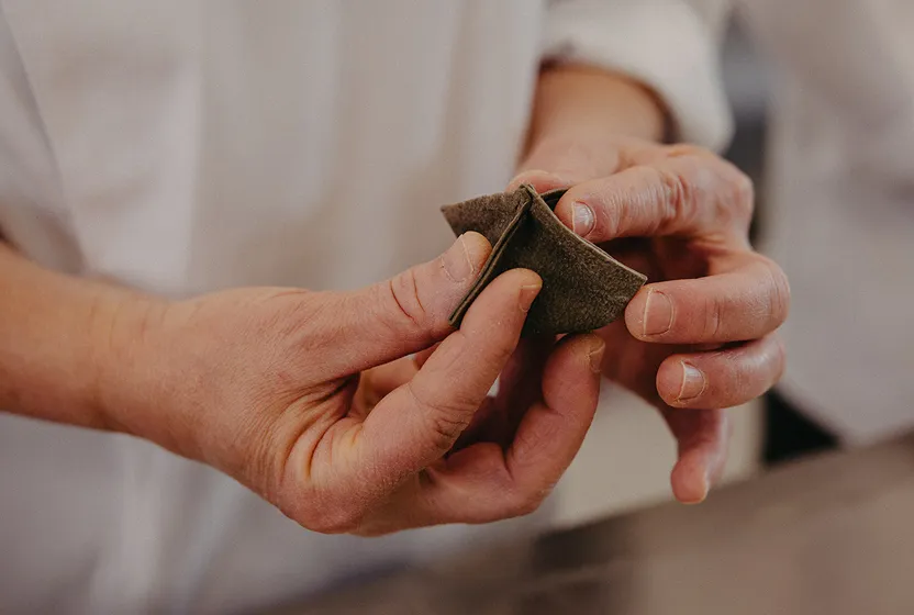 Close-up of hands folding dark pasta dough into a triangular shape.