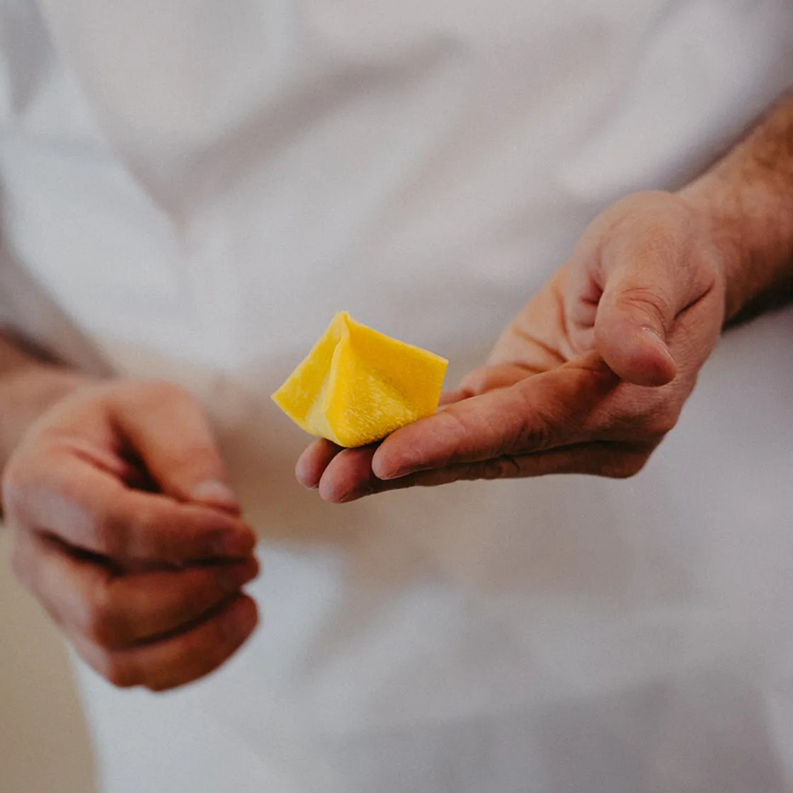 Close-up of a person holding a piece of fresh yellow pasta triangle in one hand.