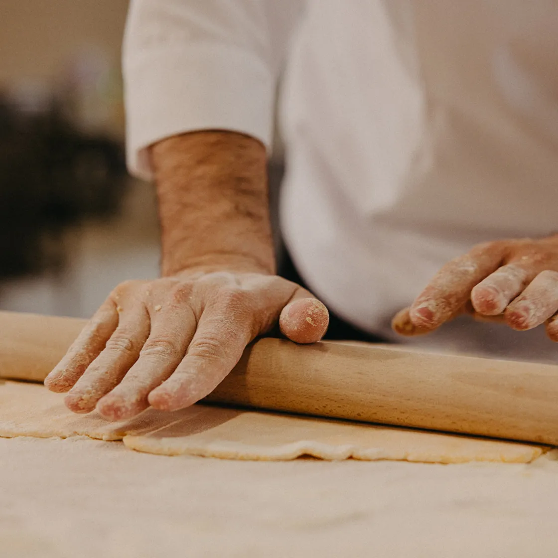 Close-up of hands dusted with flour rolling out dough with a wooden rolling pin.
