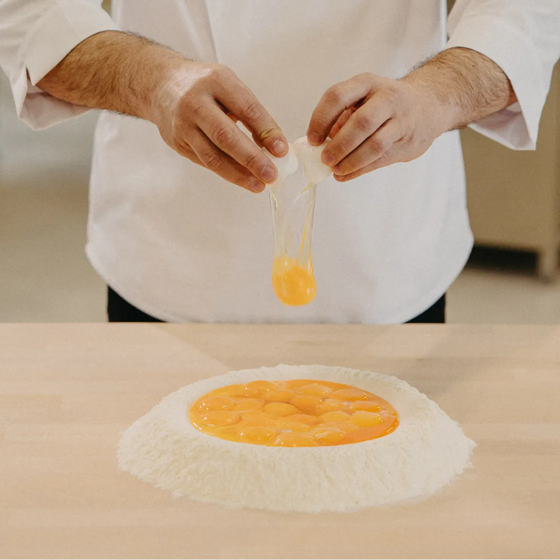 Person cracking an egg into a well of flour on a wooden surface, preparing to make dough.