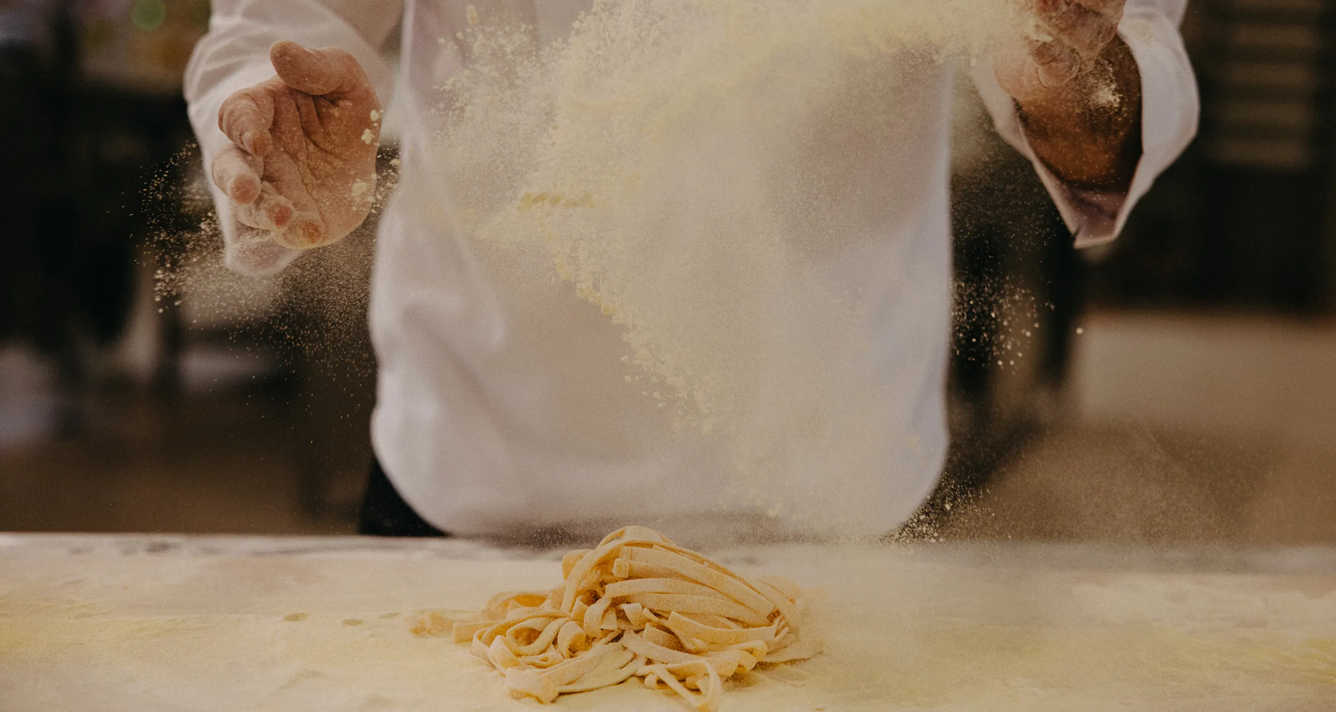 Hands sprinkling flour over fresh pasta dough on a floured surface.