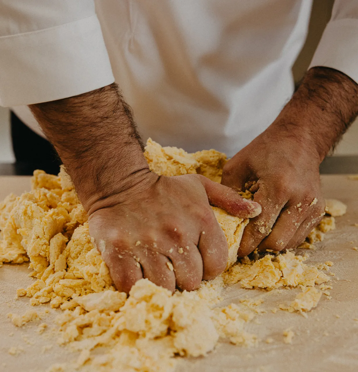 Hands kneading crumbly dough on a floured surface.