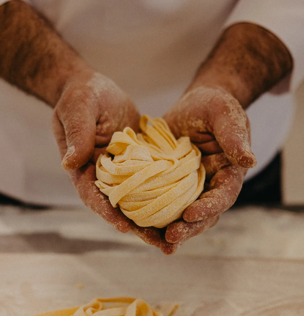 Close-up of hands covered in flour holding freshly made nest of tagliatelle pasta.