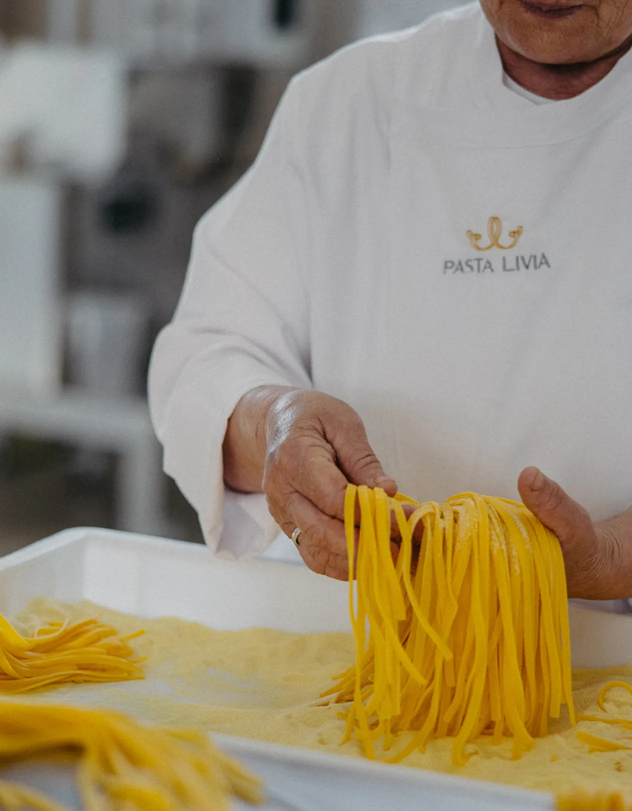Person wearing a Pasta Livia uniform holding fresh handmade pasta over a tray with more pasta.