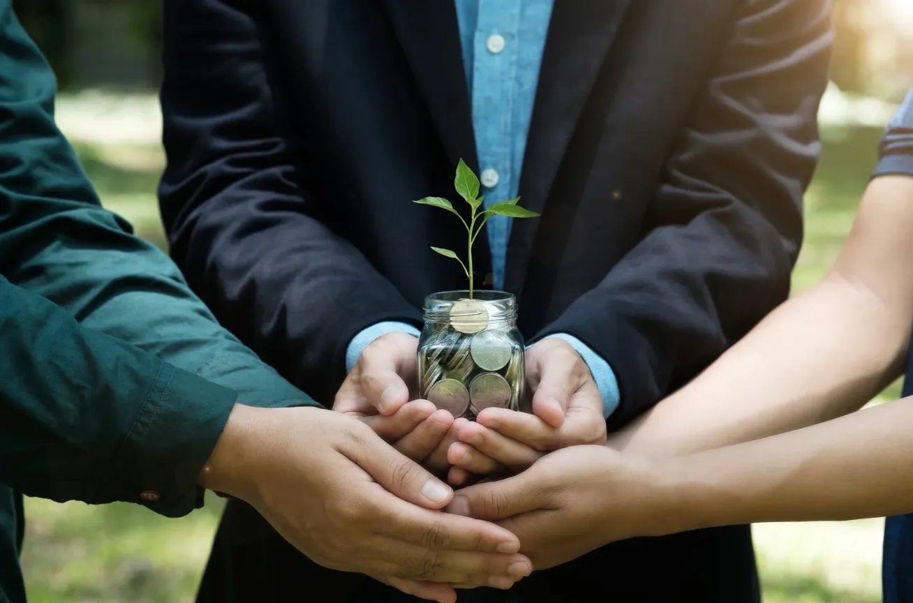 Photo de personnes qui tiennent un pot d'argent avec des pièces et une pousse d'herbe