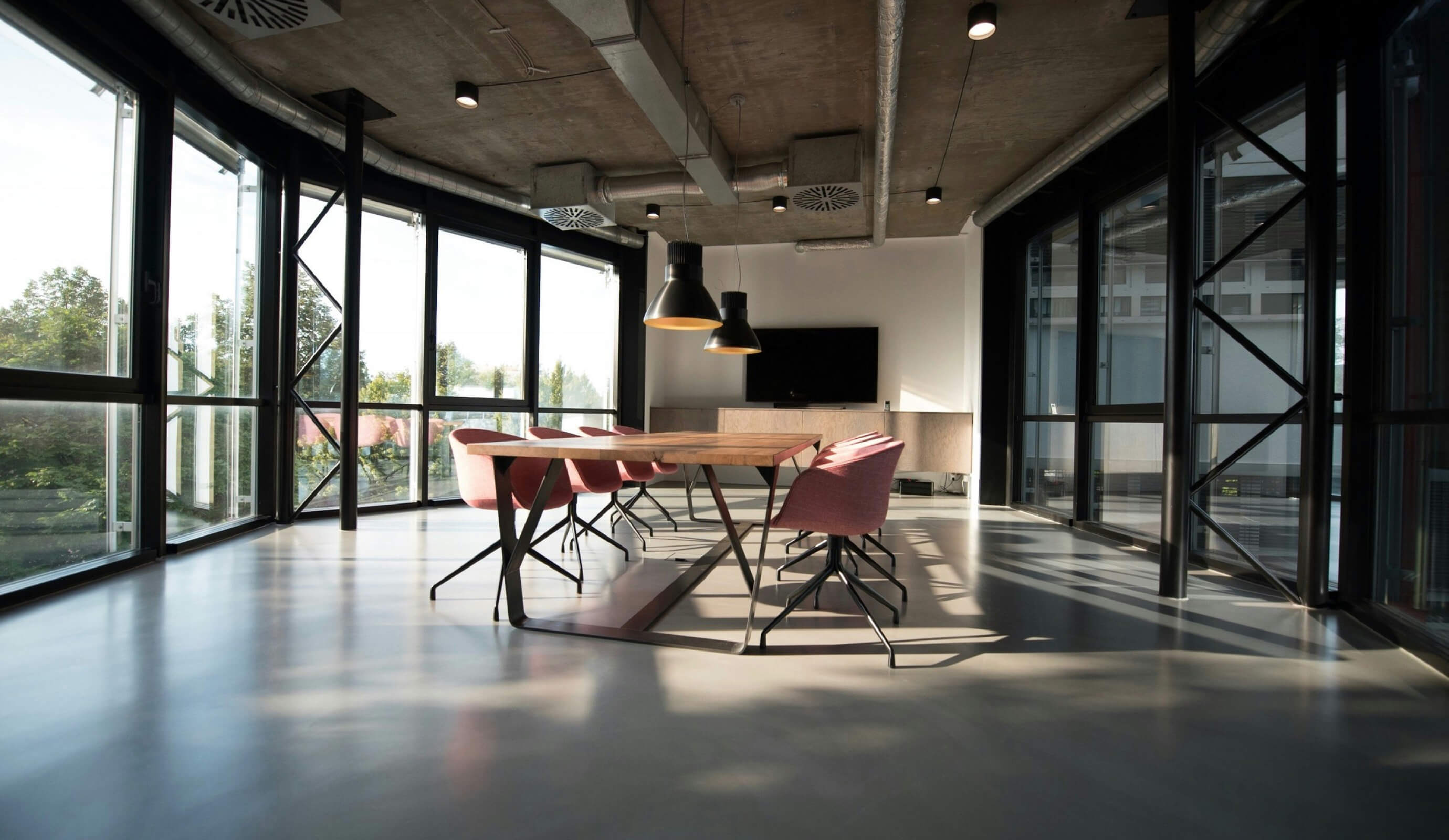 Commercial Interiors – open-plan office with a long wooden table behind a glass facade