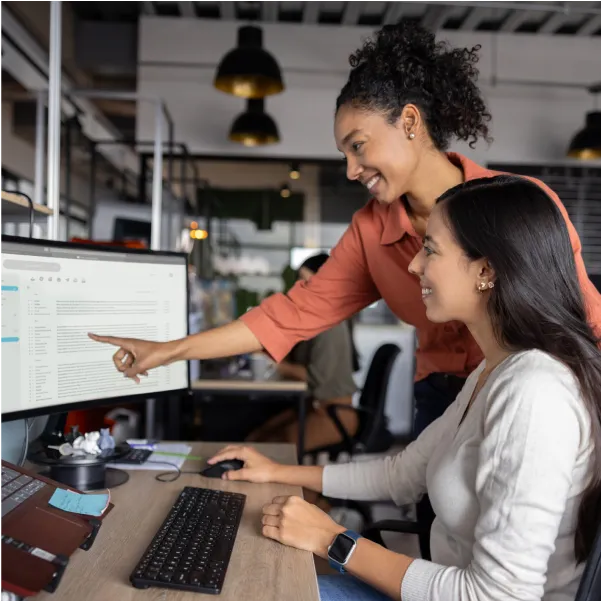 Two women sitting in front of a computer screen.