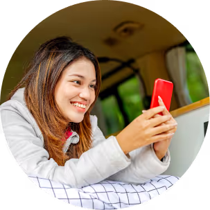 A woman smiles while seated in a van, engaged with her phon