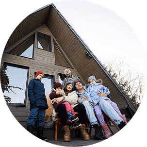 A family sitting together on the porch of an A-frame house, enjoying a sunny day together